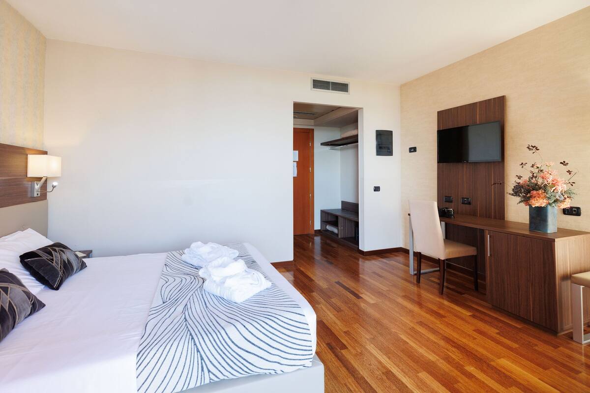 Ein Hotelzimmer mit Bett, Schreibtisch, Sessel, Fernseher und einem durchgegangenen Tür sichtbaren Badezimmer.