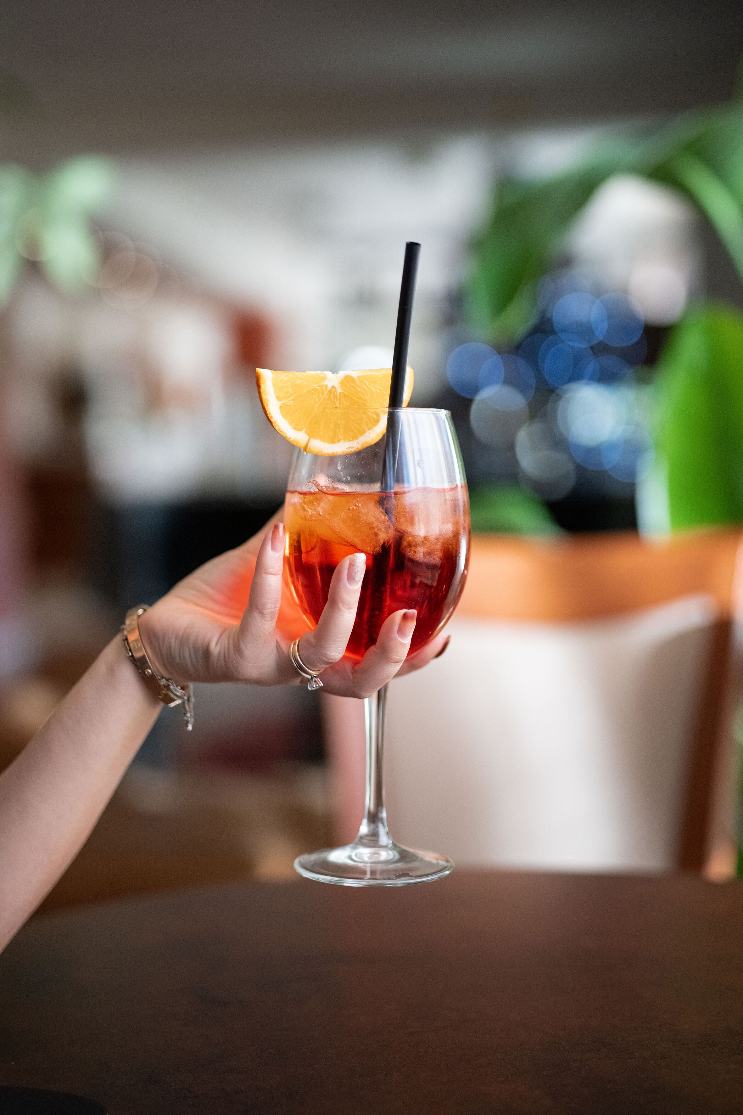 A hand holding a glass with a drink, a straw, and an orange slice.