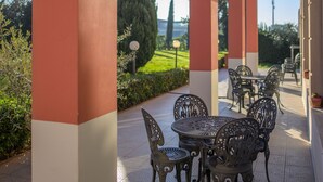 An outdoor patio with a table and chairs, surrounded by columns, with a view of greenery and distant hills. - Charme (Prato)