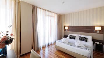 Habitación de hotel con una cama grande, una mesita de noche, una silla y una ventana con cortinas.