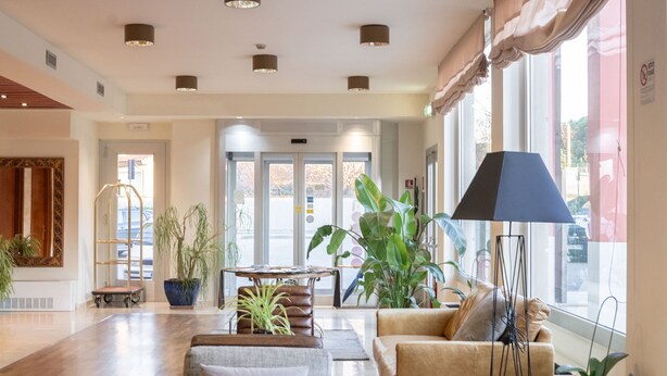 A spacious lobby with leather sofas, a coffee table, and potted plants. - Charme (Prato)