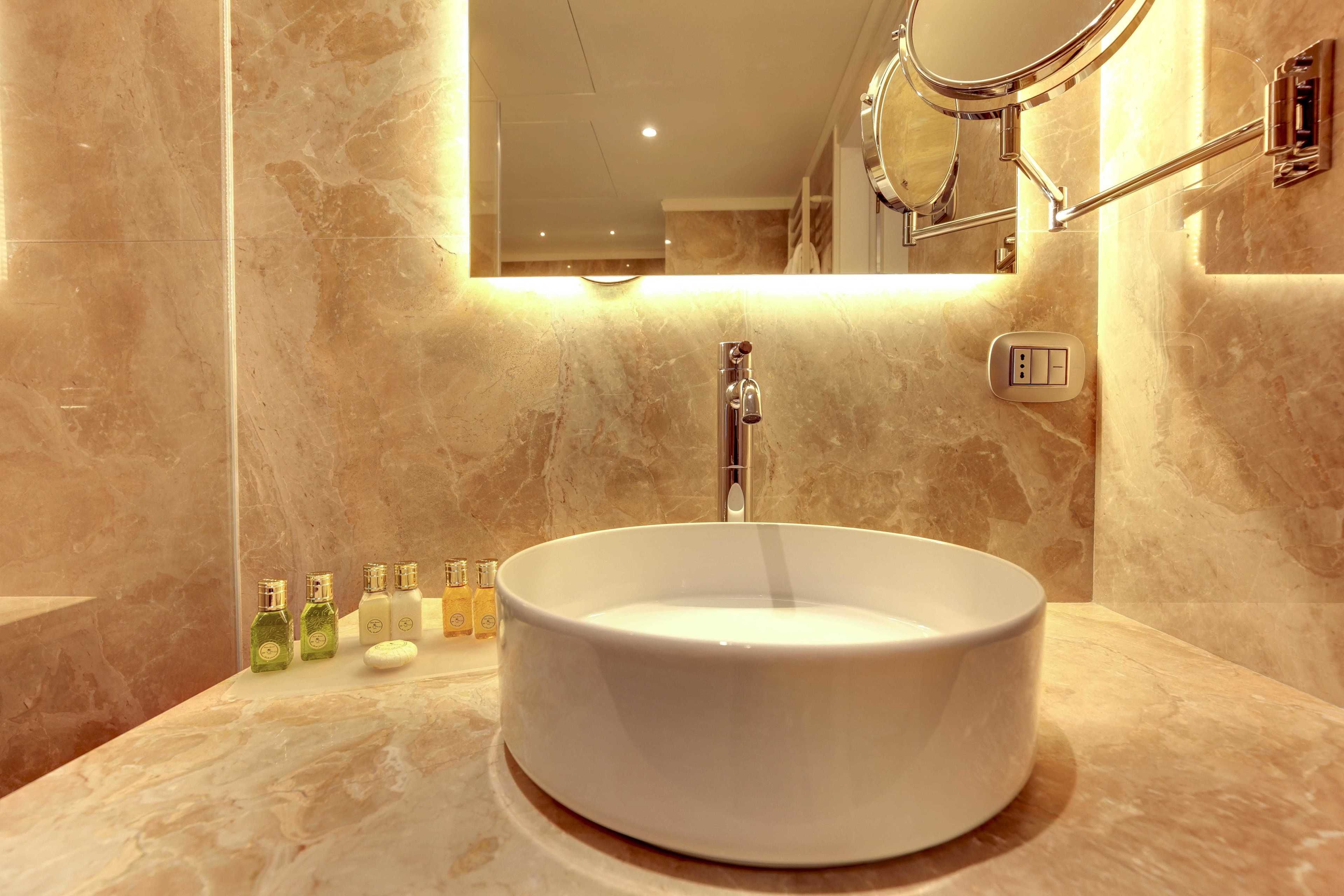 Une salle de bain avec un lavabo rond blanc, un miroir et un luminaire fixé au mur.