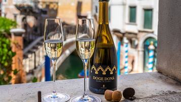 Una bottiglia di vino e due bicchieri su un balcone con vista su un canale e palazzi.