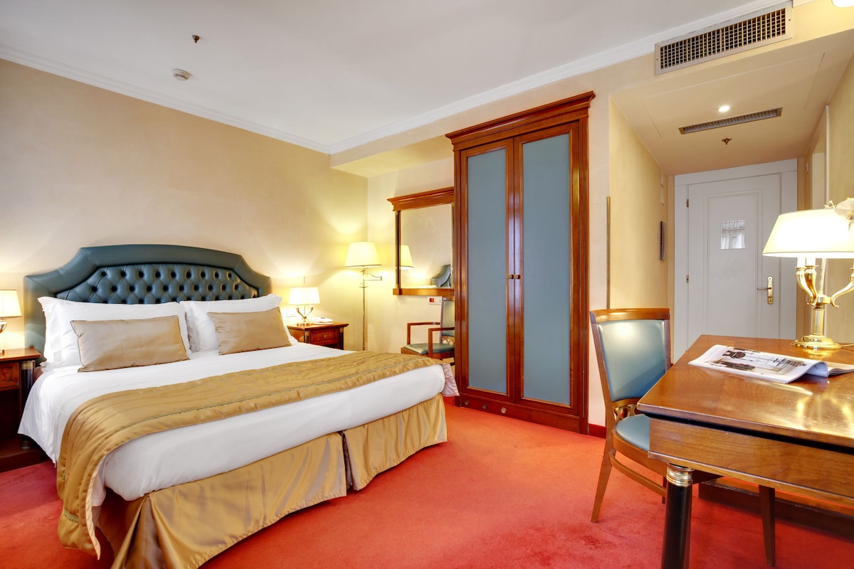 Una habitación de hotel con una cama grande, un escritorio de madera, una silla y un armario.