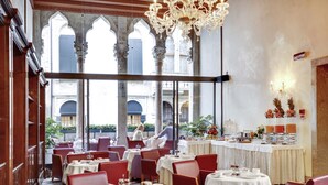 Un restaurant avec des chaises rouges et des tables blanches, de grandes fenêtres et un lustre.