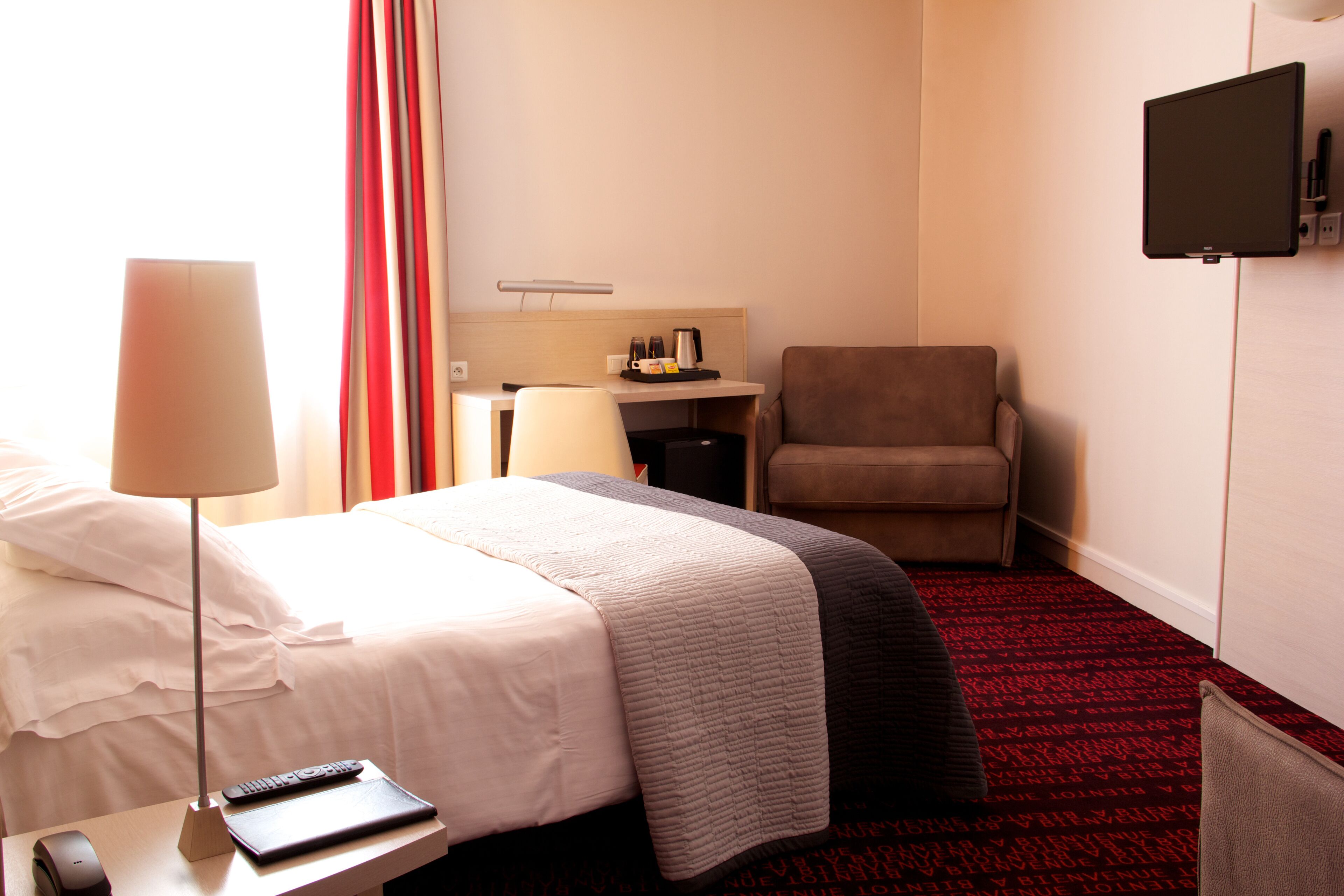 Habitación de hotel con cama, escritorio, silla, televisor, lámpara y control remoto.