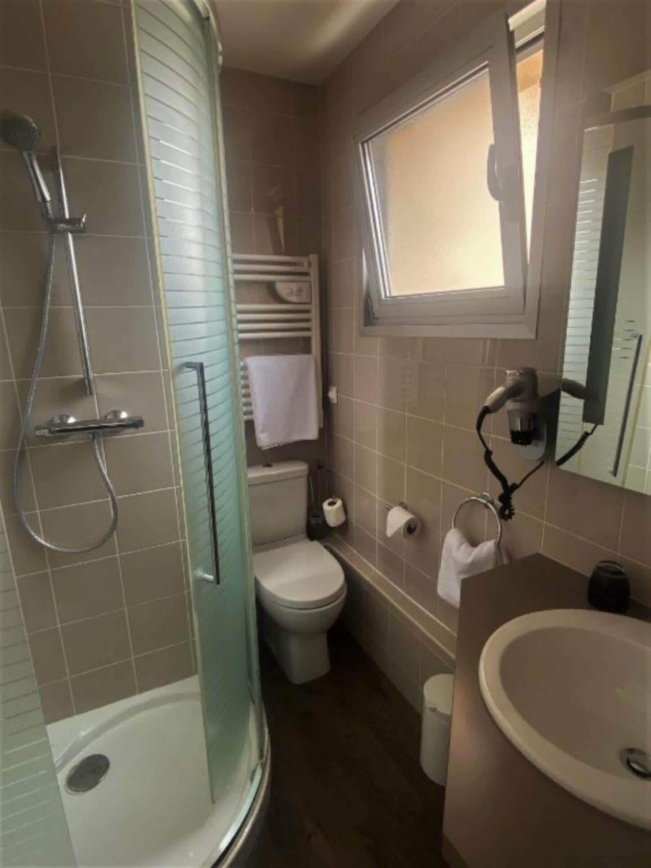 A bathroom with a shower, toilet, sink, and a window.