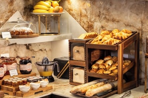 A breakfast buffet with various breads, pastries, and fruits.