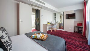 A hotel room with a bed, breakfast tray, desk, chair, TV, and a red carpeted floor. - Hôtel Le Richemont (Paris)