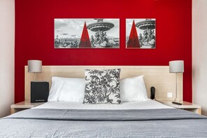 A hotel room with a red accent wall, a bed with white bedding, two pillows, a nightstand with a lamp, a phone, and a 'Guest Information' box. - Hôtel Le Richemont (Paris)