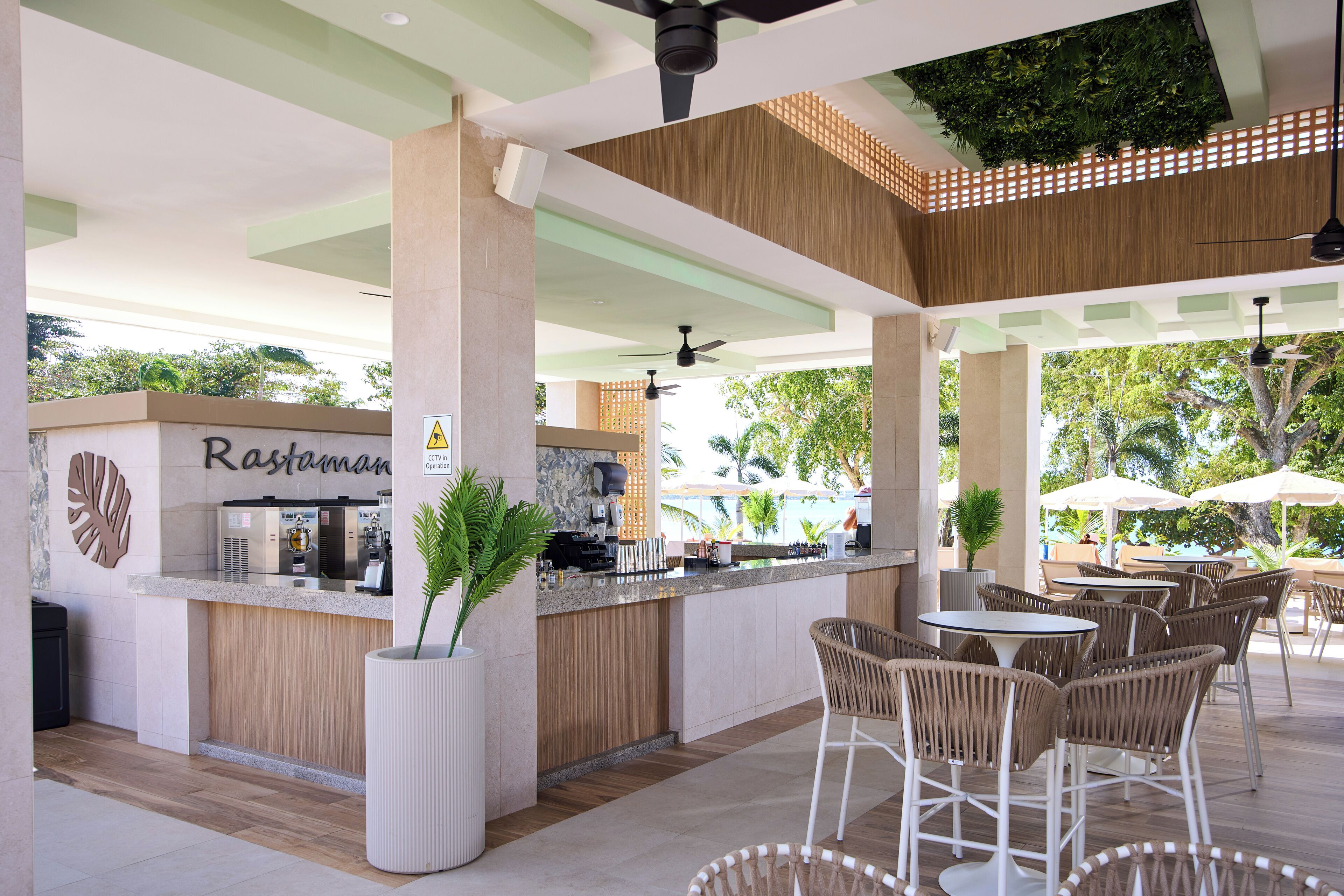 A modern outdoor bar area with seating, a reception desk, and a view of the pool.