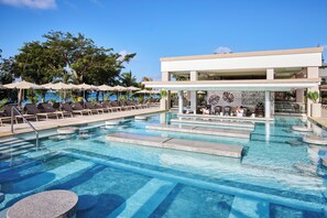 A swimming pool with lounge chairs and umbrellas, a bar area, and a building with a modern design.