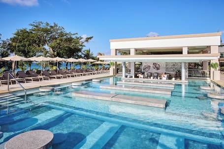 A swimming pool with lounge chairs and umbrellas, a bar area, and a building with a modern design.