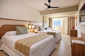 A hotel room with two beds, a ceiling fan, a TV, and a window with curtains.