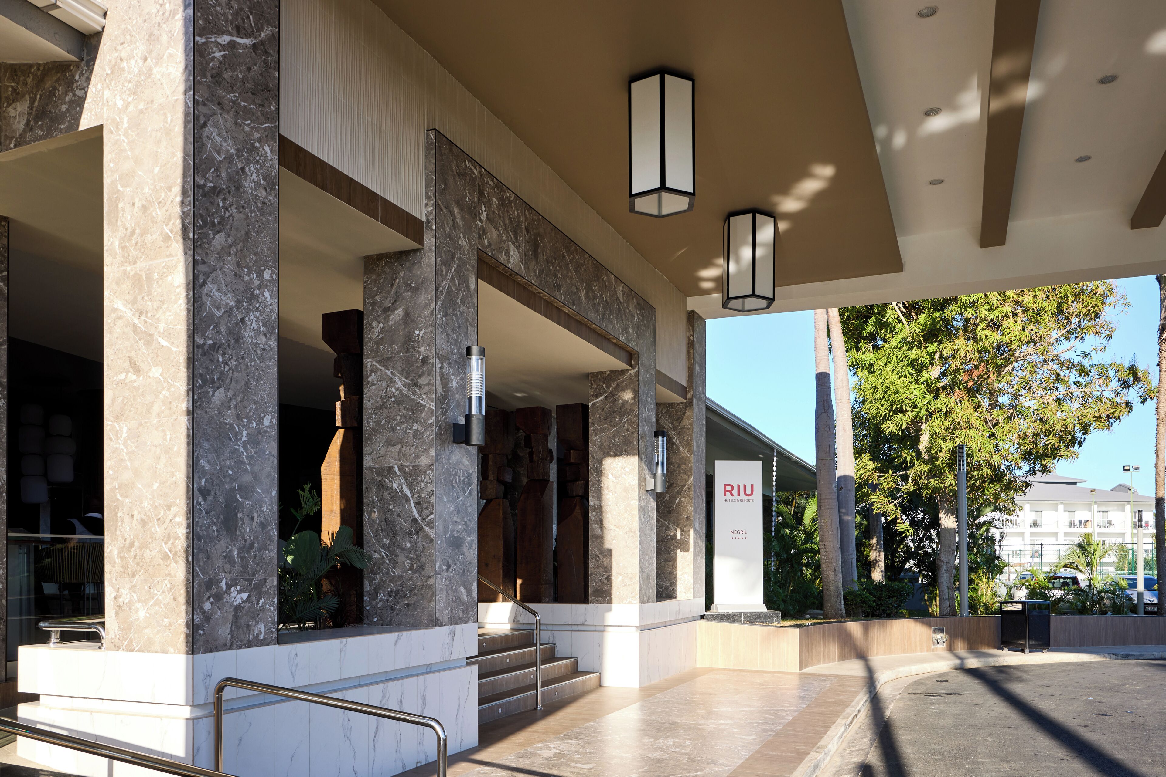 A modern hotel entrance with marble columns, a staircase, and a sign for Riu hotel.
