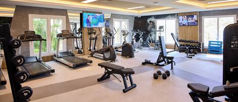 Un gimnasio con cintas de correr, elípticas, bancos de pesas y mancuernas.
