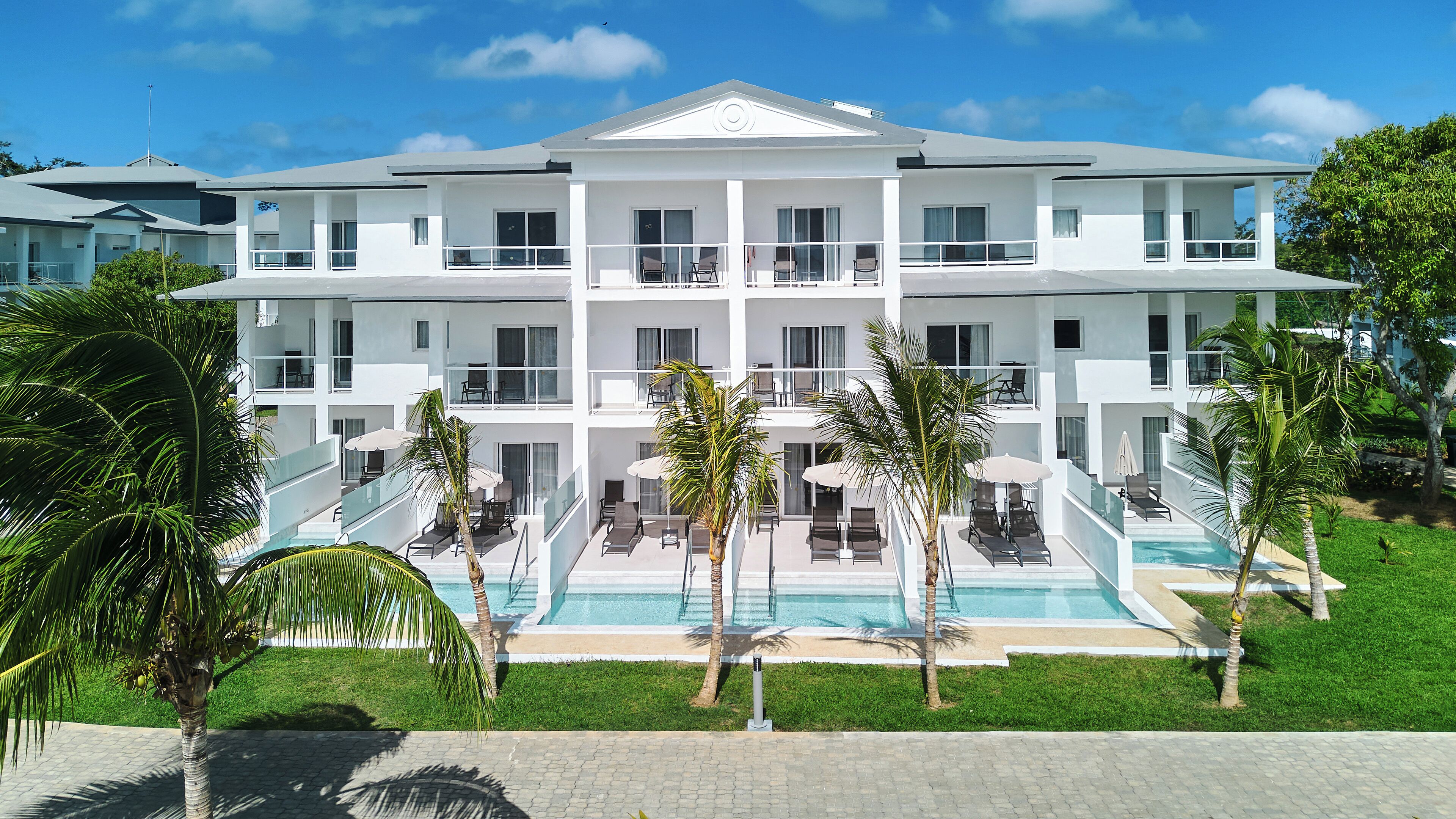 A multi-story hotel with a pool, outdoor seating, and palm trees.