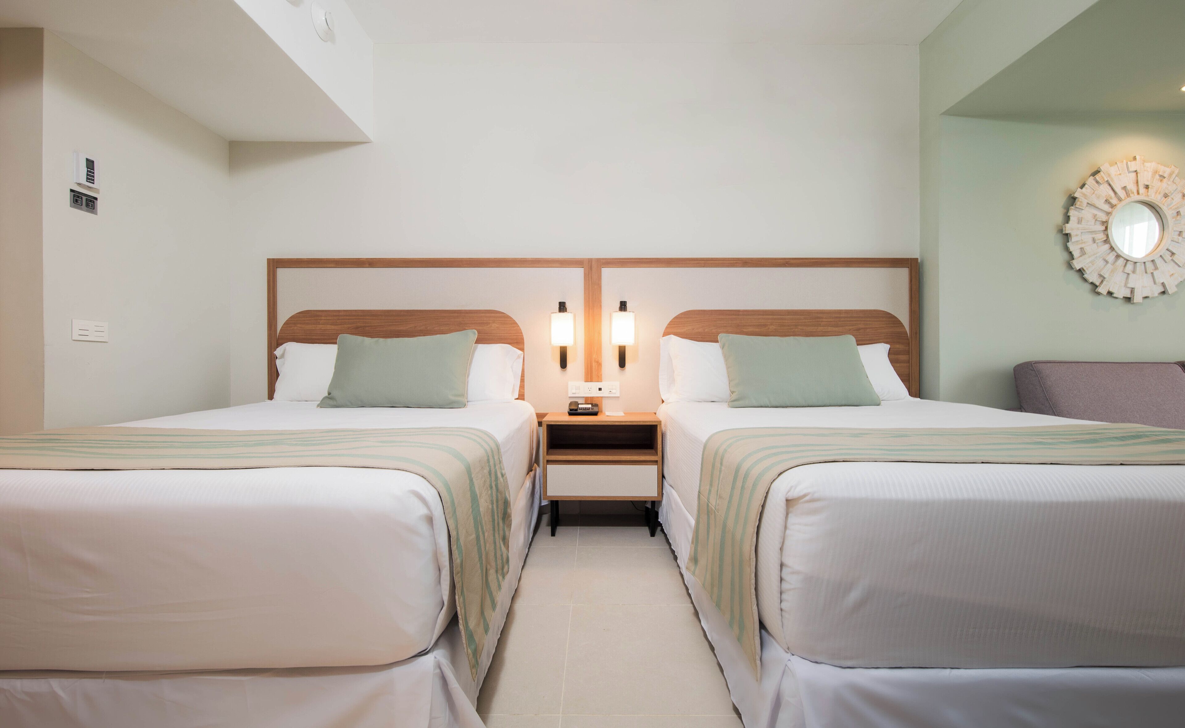 Ein Hotelzimmer mit zwei Betten, einem Nachttisch, einer Wandleuchte und einem dekorativen Spiegel.