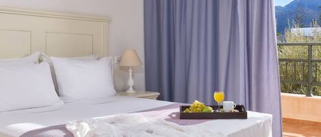 Une chambre d’hôtel avec un lit, un plateau avec des fruits et une boisson, une lampe et une vue sur les montagnes.