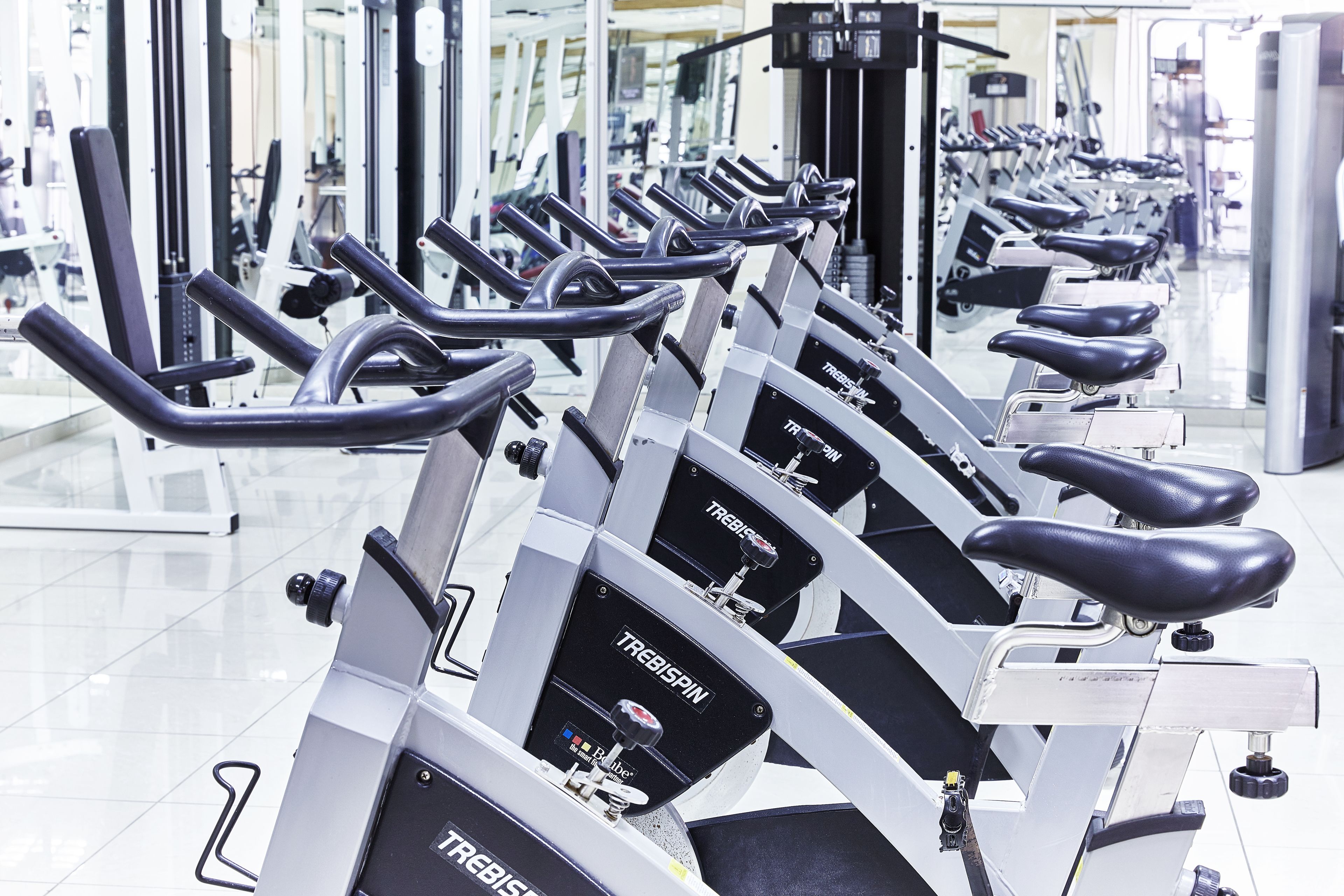 A row of stationary bikes in a gym with mirrored walls.