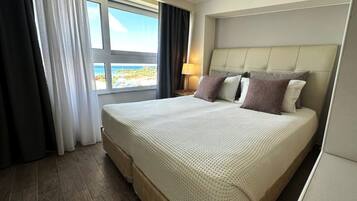 Ein Hotelzimmer mit einem großen Bett, Meerblick und einem Vorhangfenster.