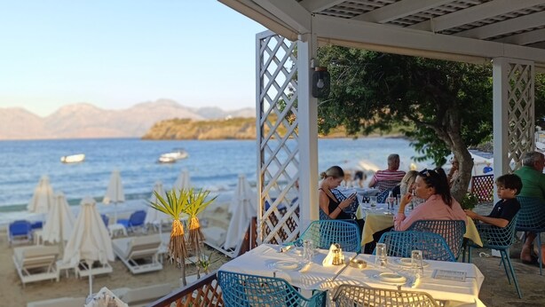 A beachside restaurant with outdoor seating, tables, and umbrellas. - Faedra Beach Hotel (Agios Nikolaos)