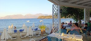 A beachside restaurant with outdoor seating, tables, and umbrellas. - Faedra Beach Hotel (Agios Nikolaos)
