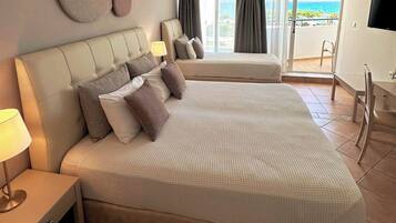 A hotel room with a large bed, a smaller bed, a TV, and a balcony with a view of the sea.