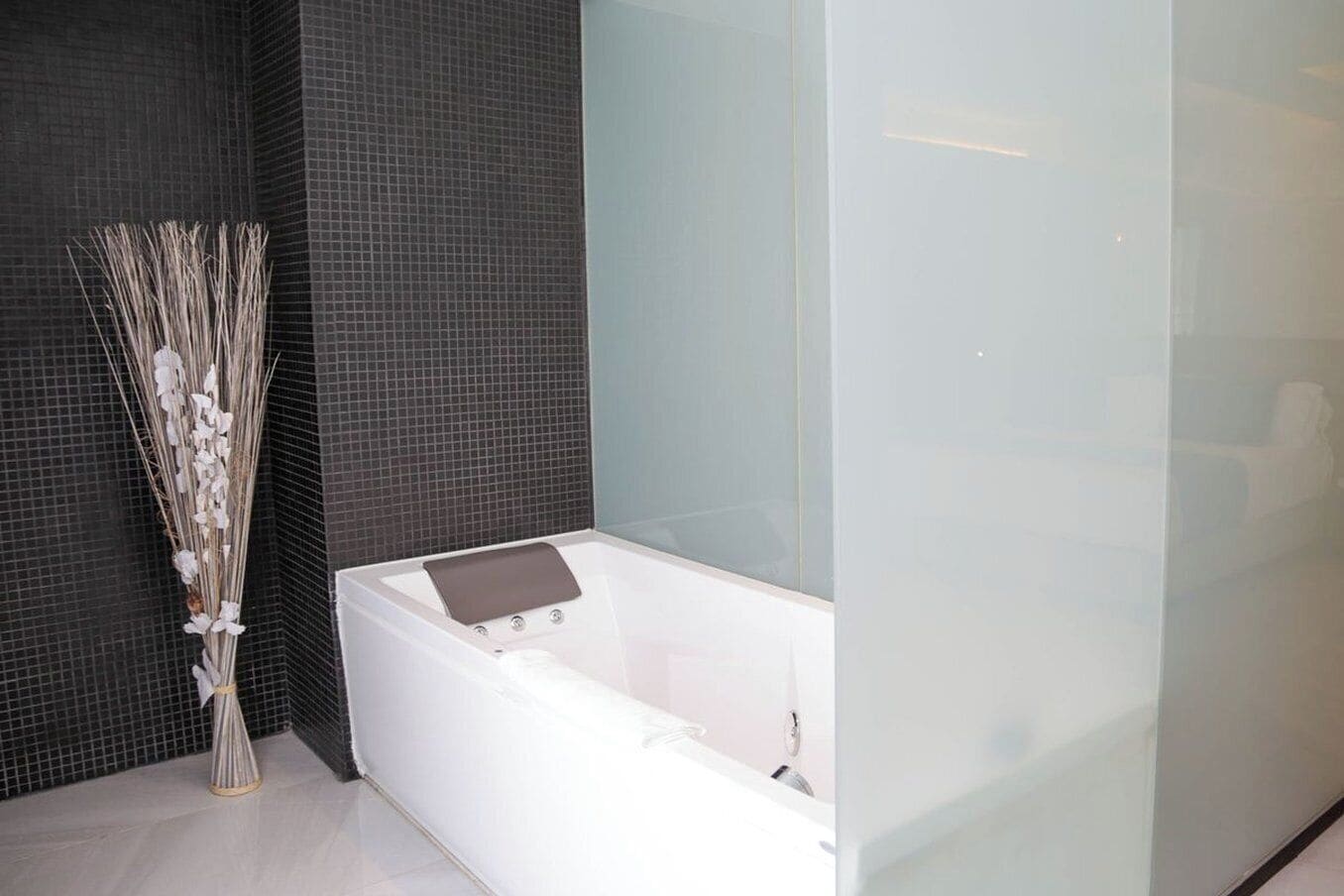 Un baño moderno con una bañera blanca, paredes cubiertas de azulejos oscuros y un cerramiento de ducha de vidrio transparente.