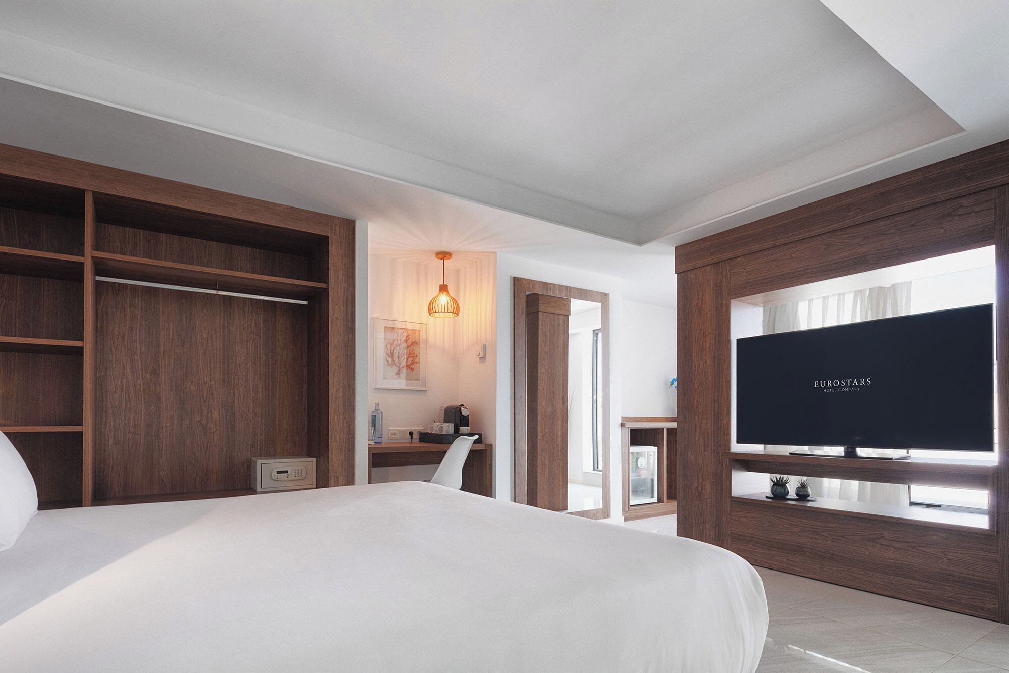 Habitación de hotel con una cama grande, un armario de madera, un televisor y vistas a través de una ventana.