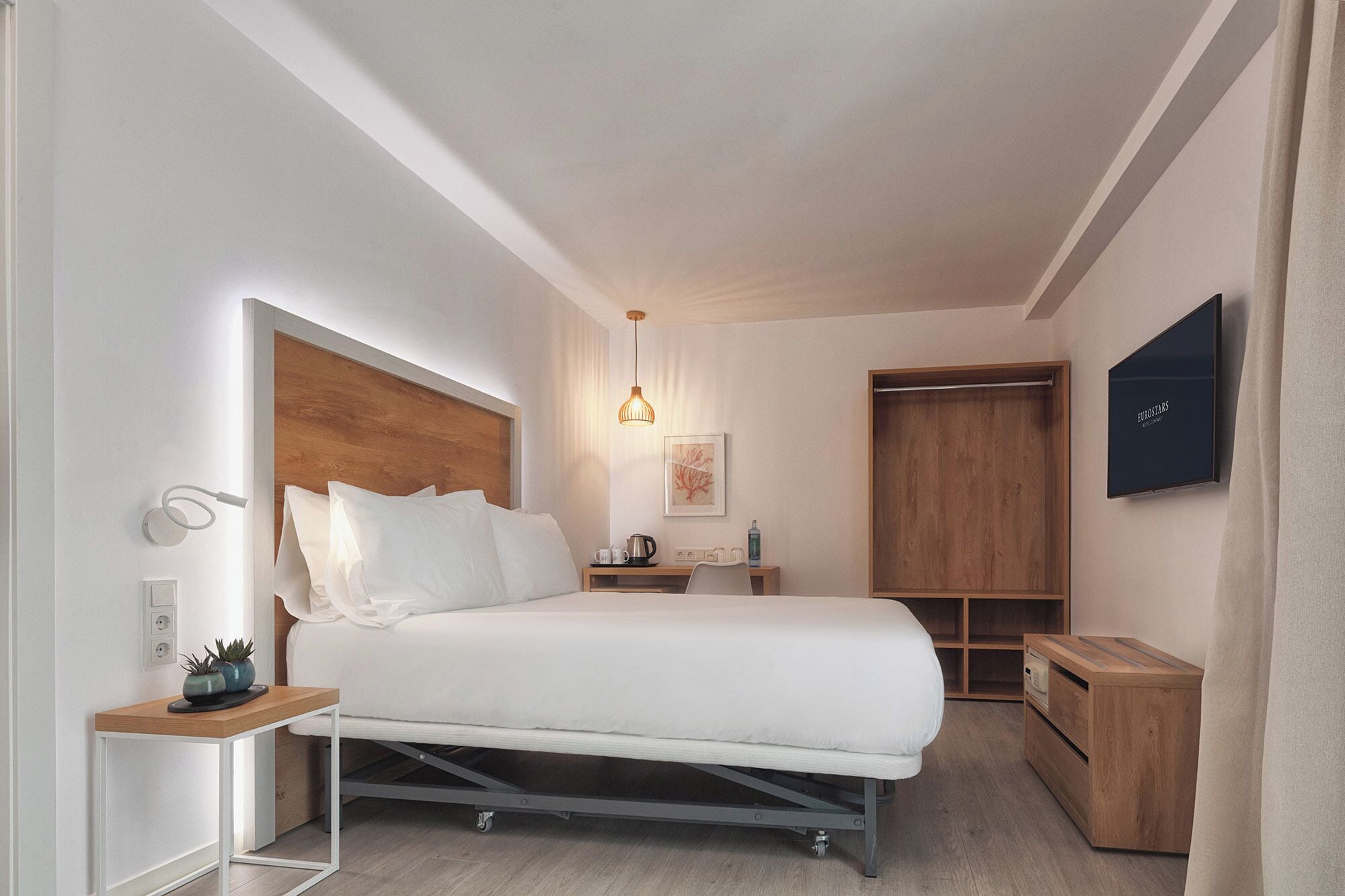 Una habitación de hotel moderna con una cama, mesita de noche, lámpara y un televisor fijado en la pared.
