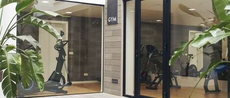 A modern gym with exercise equipment, large windows, and indoor plants.