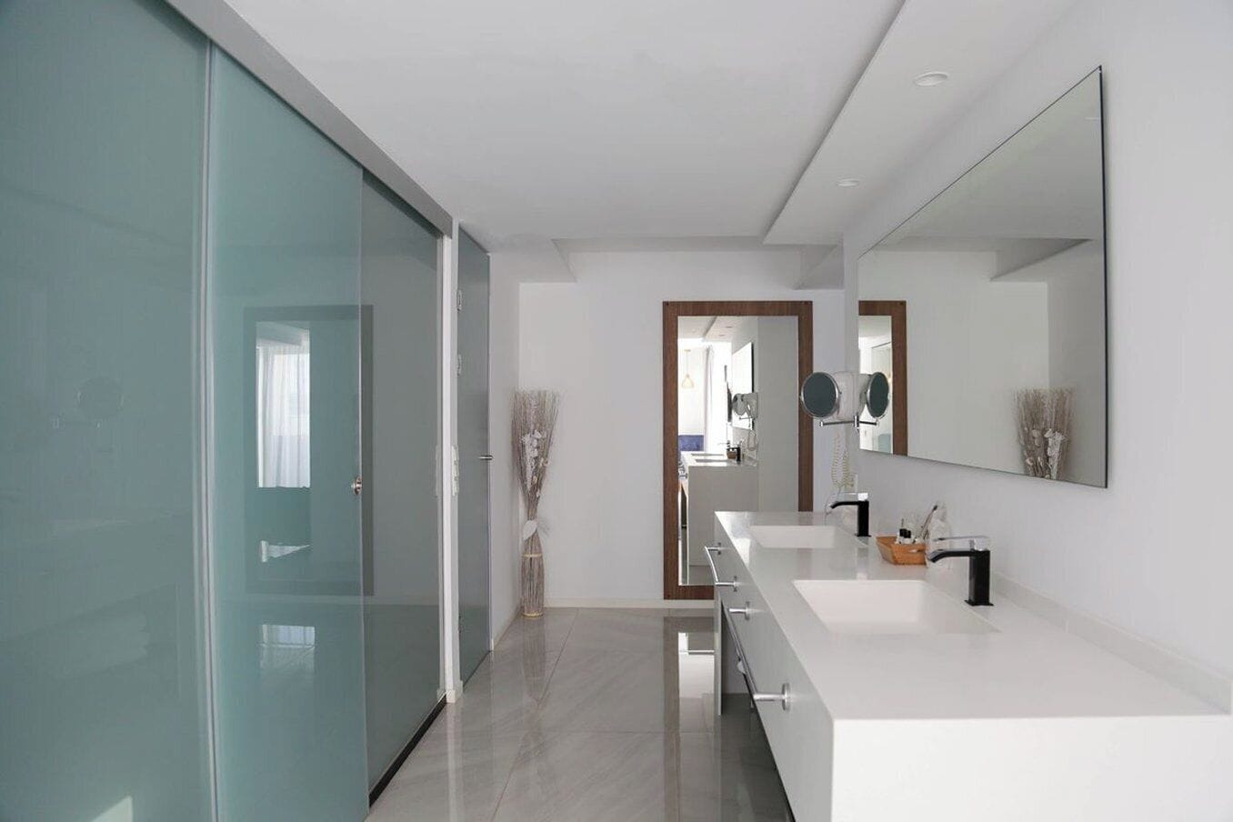 A modern bathroom with a glass door, a large mirror, and a white countertop.