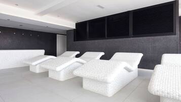 Un spa moderno con tres sillones blancos y texturizados, y un ventanal grande con persianas negras.
