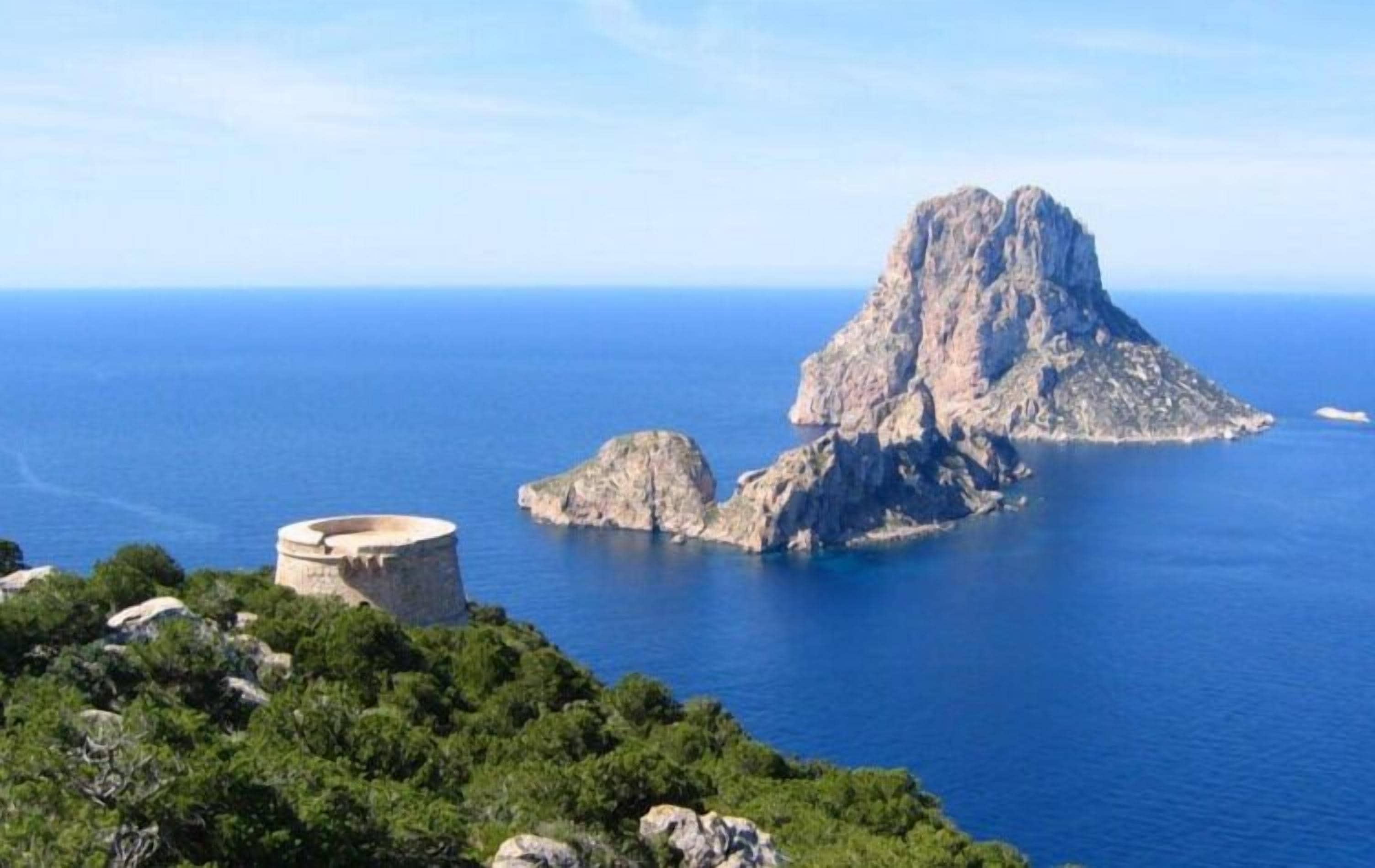 Paesaggio costiero con formazioni rocciose e una struttura circolare, probabilmente un faro, che si affaccia sul mare.
