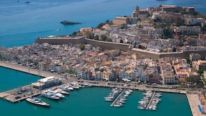 A coastal town with a fortified castle, a marina with numerous boats, and densely packed buildings.