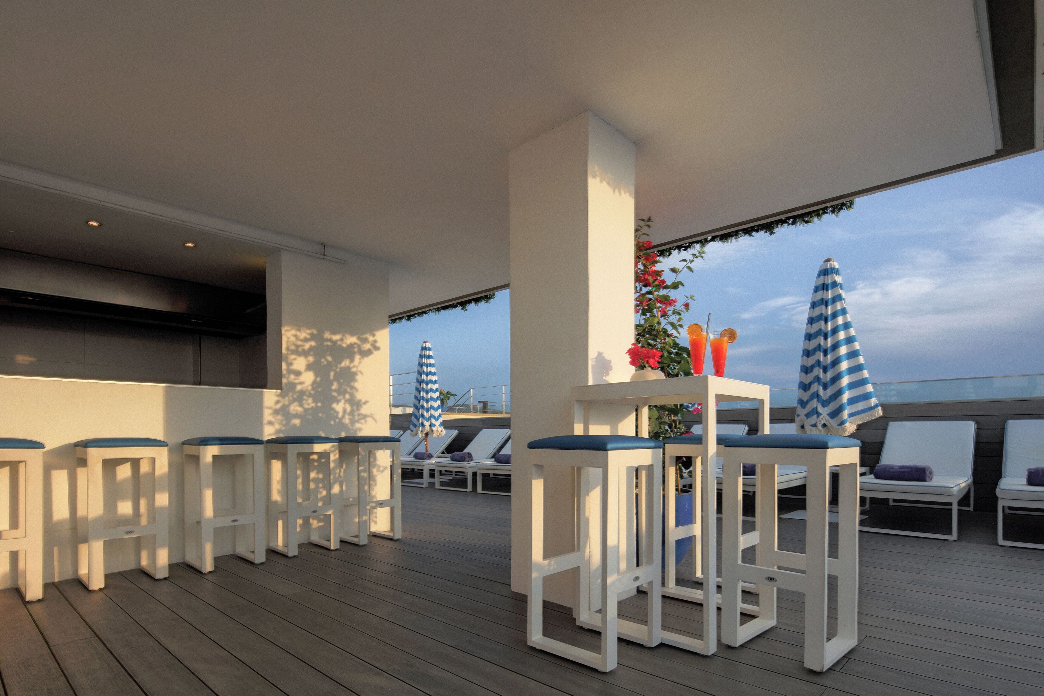 Een terras met witte barstoelen, lounge fauteuils en parasols.