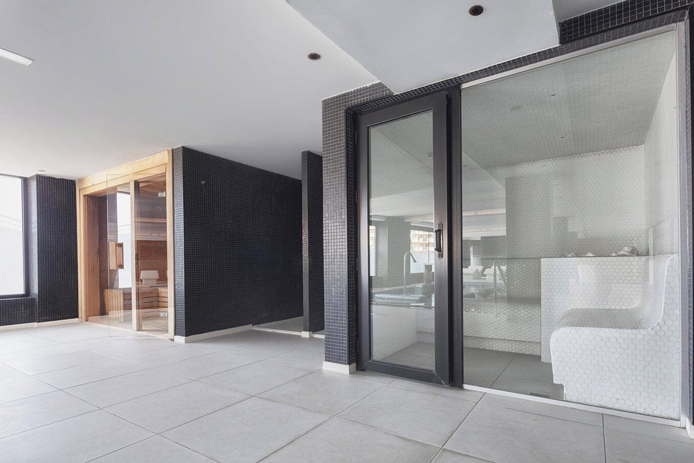 Un interior moderno con un gran ventanal corredera que da a un baño, piso de baldosas y puerta de madera.