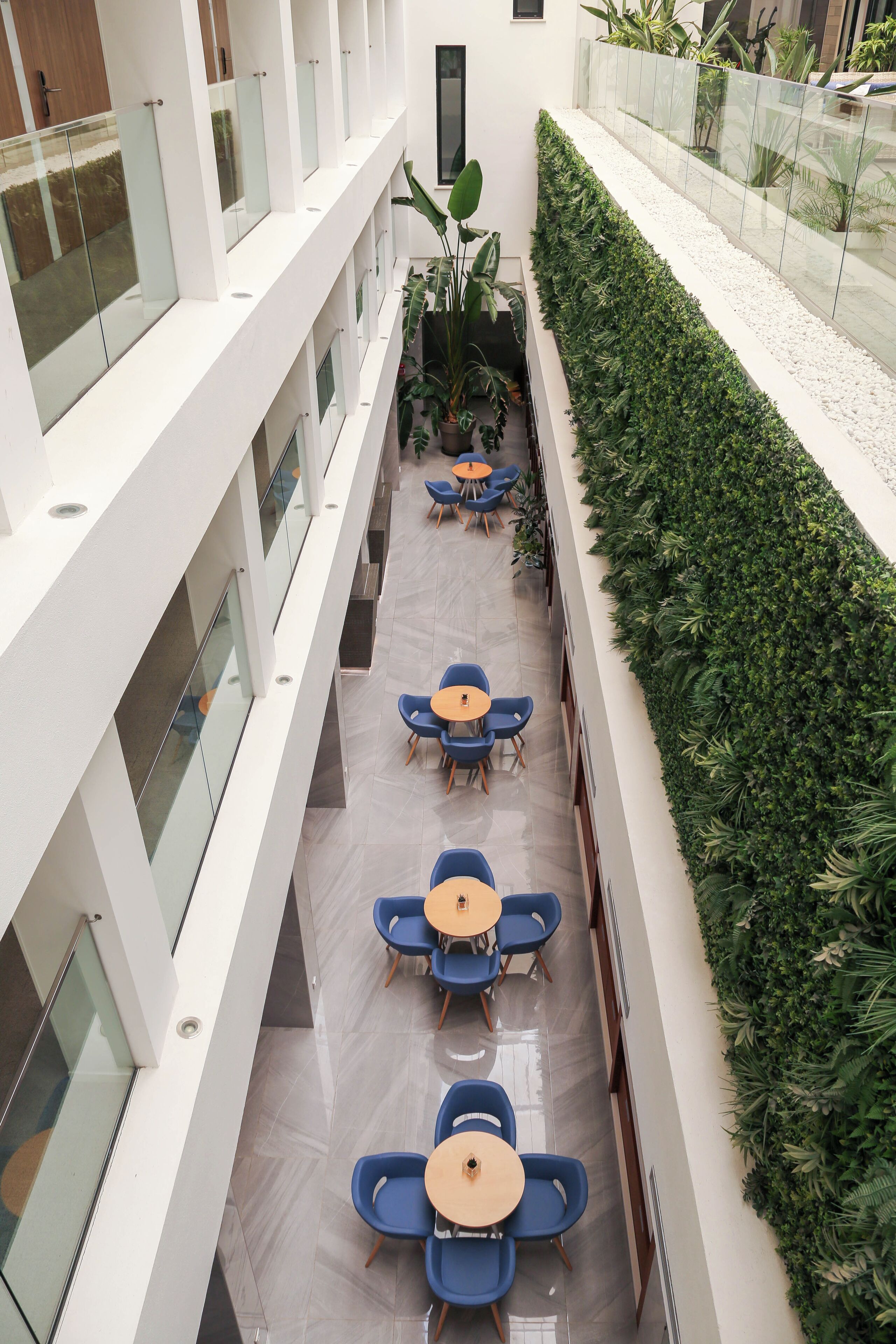 A modern indoor space with a central corridor, glass railings, and seating areas with tables and chairs.