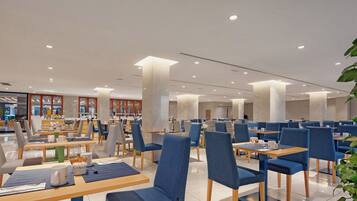 A modern dining area with multiple tables and chairs, a clean and spacious layout, and a view of the adjacent restaurant area.