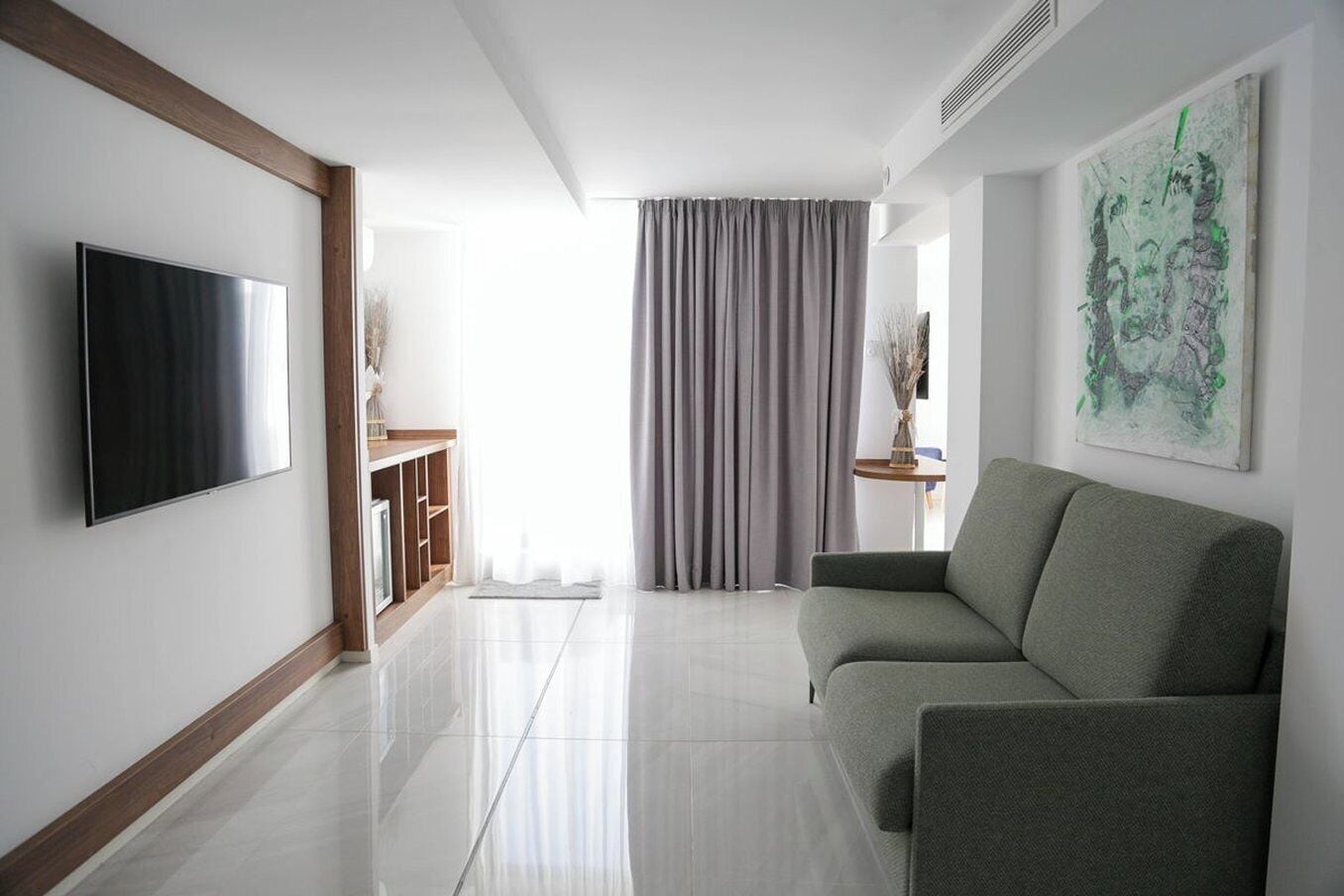 A modern living room with a flat-screen TV, a grey sofa, and a painting on the wall.