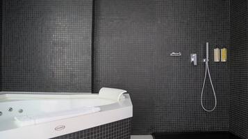 A modern bathroom with a large bathtub, a handheld showerhead, and a wall-mounted faucet.