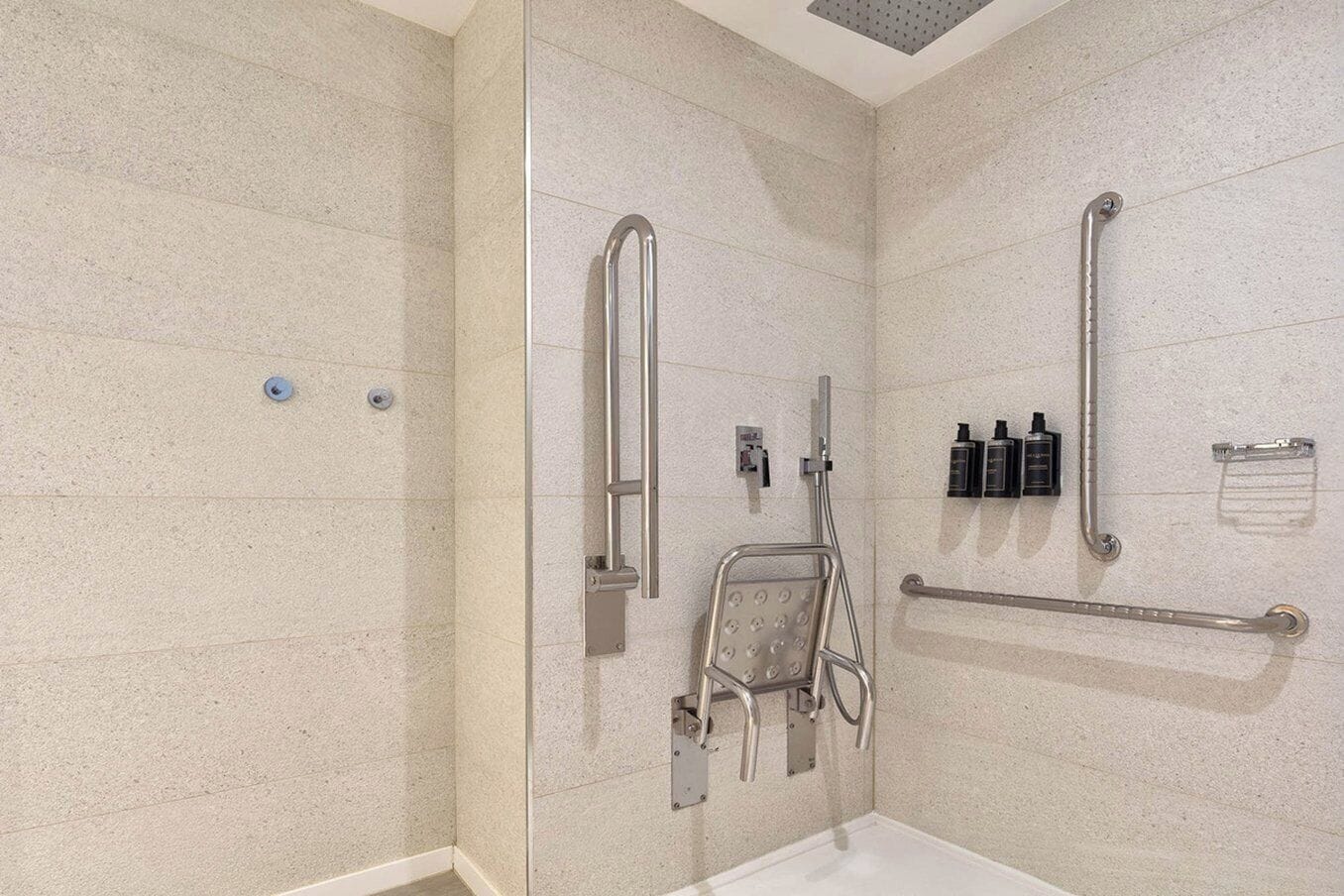 Une salle de bain moderne dotée d’une douche à l’italienne, de barres d’appui et d’un pommeau de douche amovible.