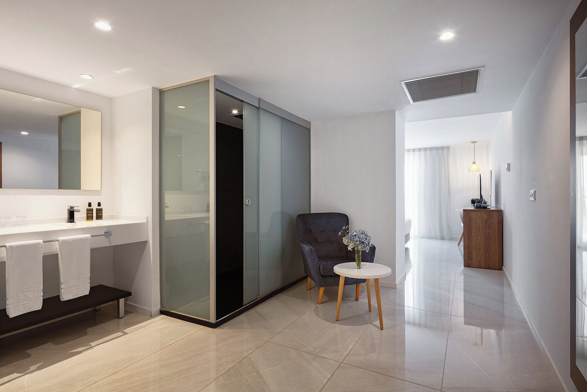 A modern bathroom with a glass shower enclosure, a vanity with a mirror, and a round table with a vase.