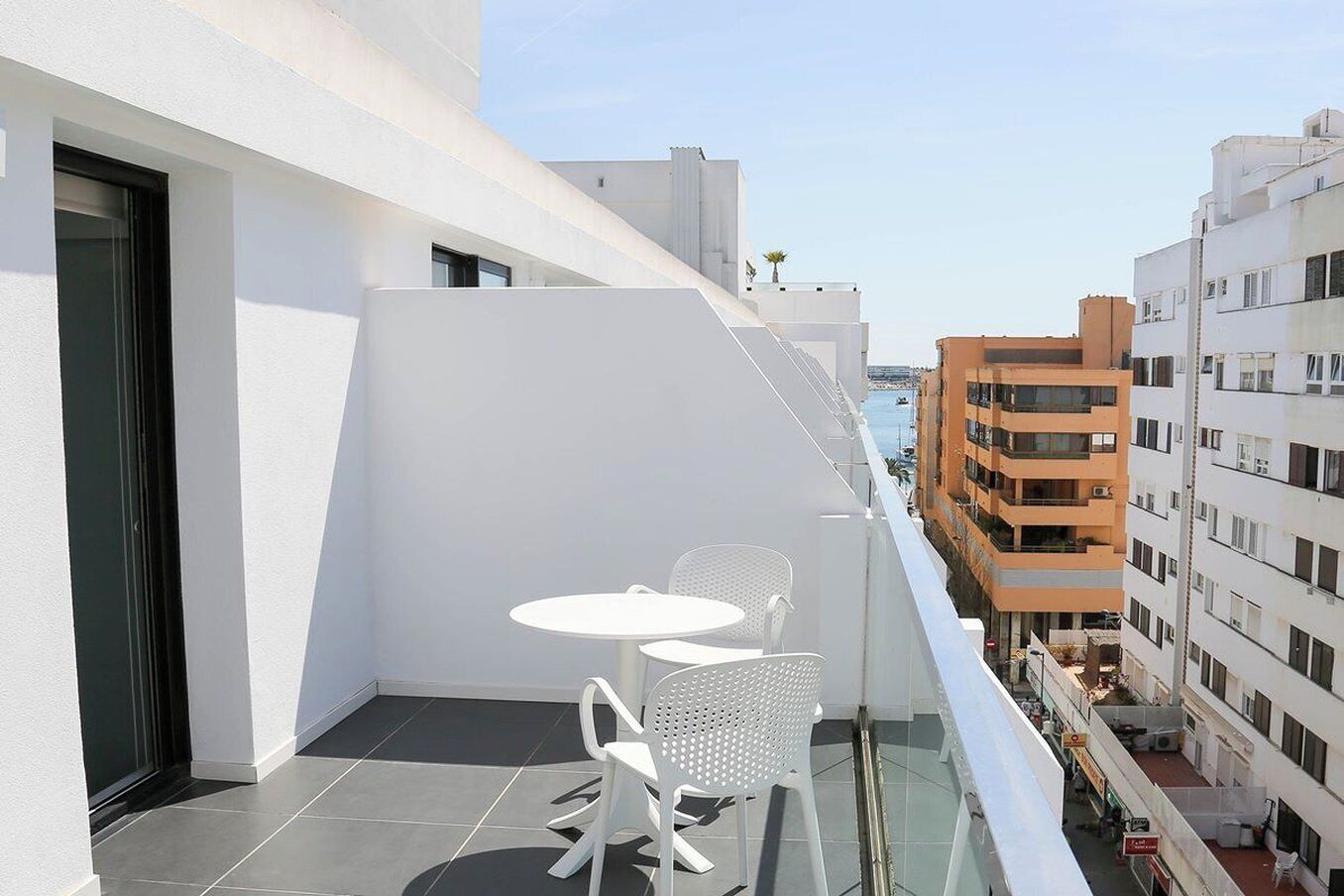 A balcony with a table and chairs, overlooking a cityscape with buildings.