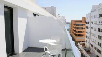 A balcony with a table and chairs, overlooking a cityscape with buildings.