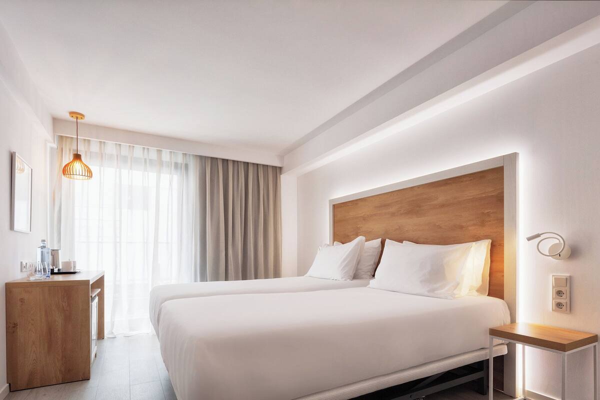 Une chambre d’hôtel avec un grand lit, une tête de lit en bois, une table de chevet et un luminaire suspendu.