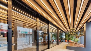 A modern building with a glass facade, wooden slats on the ceiling, and indoor plants.