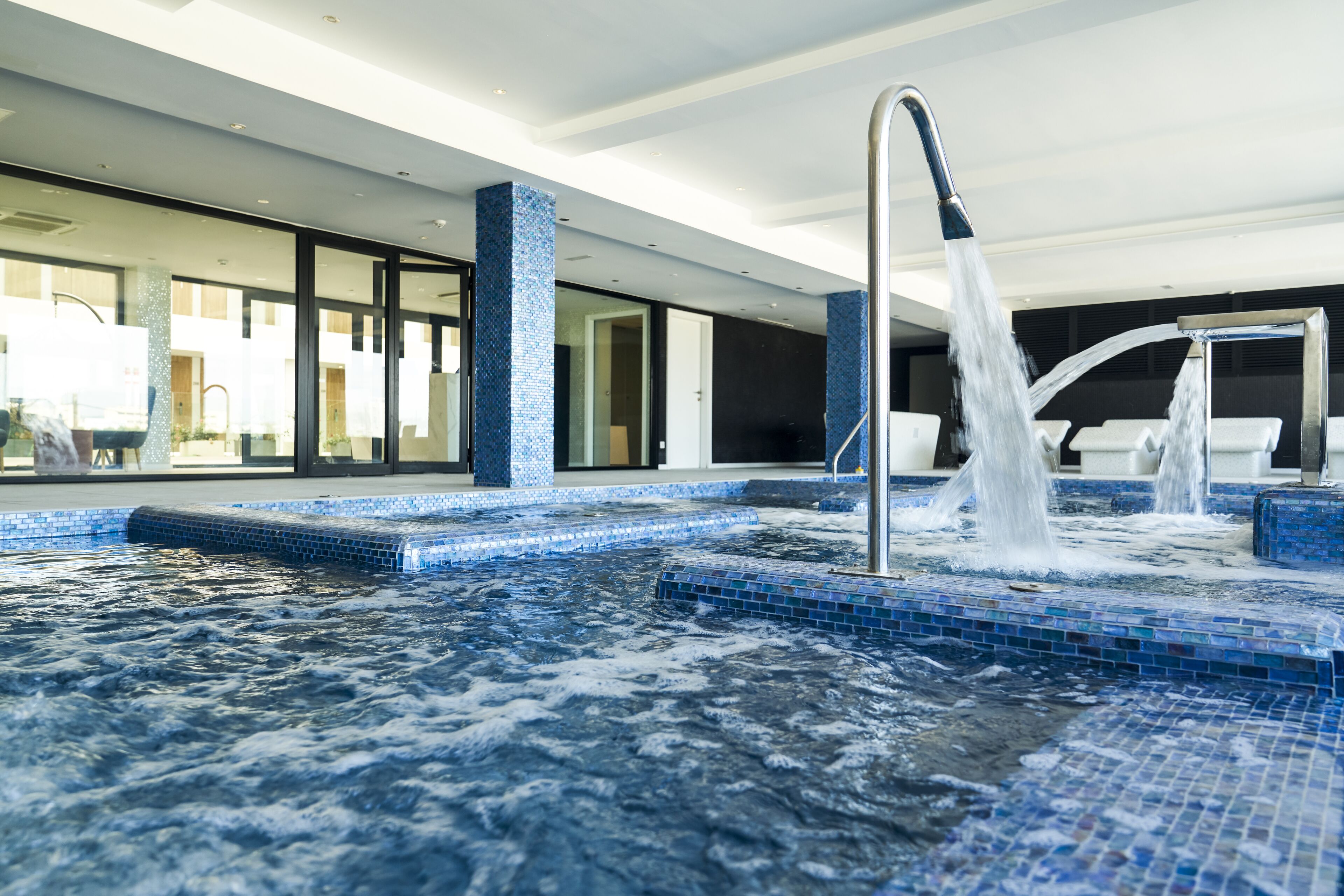 A modern indoor pool area with a hot tub and a water fountain.