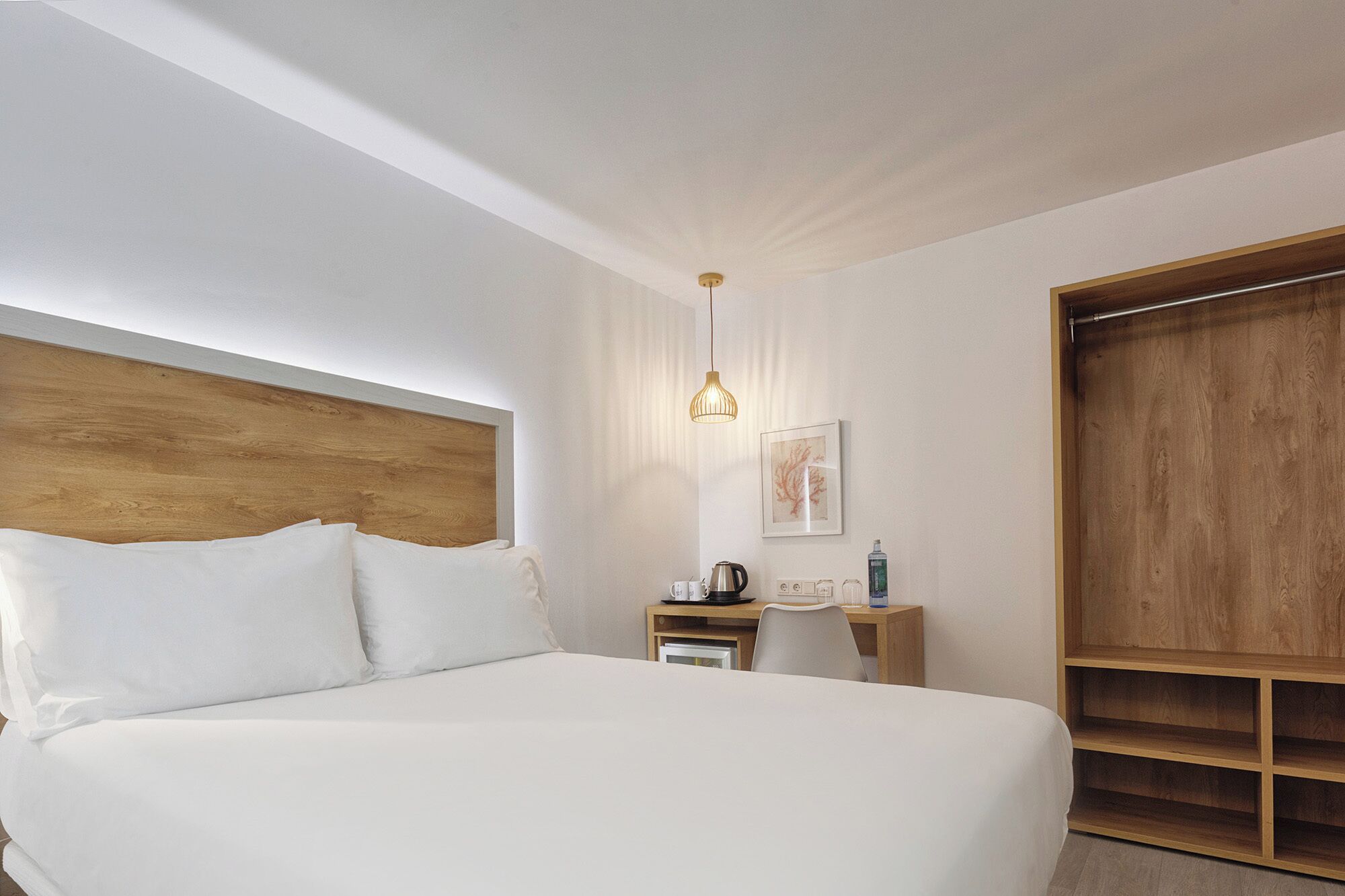 Een slaapkamer met een groot bed, een houten hoofdbord, een nachtkastje met een waterkoker, een kleine stoel en een houten garderobe.